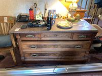 Full view of vintage hardwood dresser showing granite top, three drawers with brass handles (one missing). Items on top like plates and bottles present but not included.