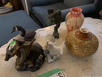 Overview photo showing all 6 items on a table, depicting two vases, several animal and figurine sculptures including a metal fox head and porcelain birds and farmer ox figurine.