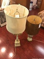 Photo showing both lamps side by side on hardwood floor; cream multi-arm lamp with cream shade and ceramic floral lamp with brown shade damaged