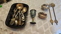 Entire lot arranged on tablecloth showing two Ronson table lighters, assorted serving utensils including spoons, ladles, forks, and a tarnished metal cup.