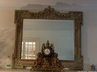 Front view of large ornate rectangular mirror with carved baroque-style frame and decorative clock statue with cherubs at base.