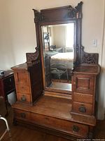 Front view of vintage wooden cabinet with large mirror, showing carved details and hardware.