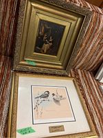 Photo showing two framed artworks: a smaller classical style painting in gold frame with some damage and peeling, and a larger framed print of birds signed Michael Dumas.