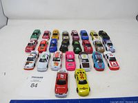 Photo showing 25 NASCAR toy cars displayed in rows on white surface, various colors and removable roof styles.