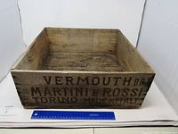 Front view of the wooden crate showing the printed text 'VERMOUTH DR MARTINI E ROSSI TORINO - MADE IN ITALY'. A blue ruler is placed in front for size reference.