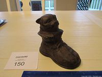 Cast iron cat in boot coin bank shown standing on table with auction number card and ruler for scale.