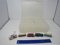 Five vintage toy vehicles displayed in a plastic organizer box, photographed with a ruler for size reference.