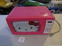 Front view of pink Hello Kitty microwave with character face on door.