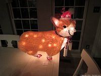 Front and side view of large light up corgi festive decoration on table, lit up in dark room.