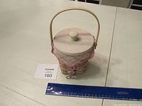 Longaberger woven basket with wooden lid, pink floral fabric liner, and handle, shown on white table with ruler for size reference.