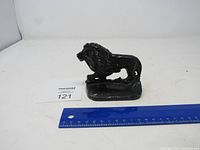 Black metal lion figurine door stop/book end shown next to a ruler for size reference indicating approximately 10 cm length.