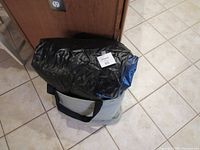 Front view of the folded black inflatable mattress packed inside the gray carrying bag on a tiled floor.