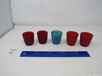 Five hobnail glasses with textured rounded bumps, including four red and one blue glass with a ruler for size reference.
