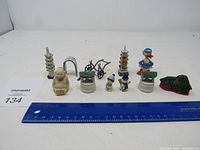 Several antique metal miniature items including seated monkey, pagodas, wishing wells, a rickshaw, duck figurine, and green roofed structure shown from front with blue ruler for scale