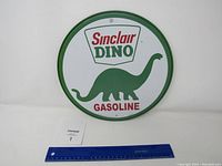 Front view of the round Sinclair Dino Gasoline metal sign with ruler for scale.