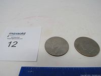Two Eisenhower Bicentennial dollar coins placed next to a ruler for size reference.