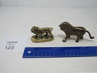 Two metal lion figurines side by side with ruler for scale and MaxSold lot number card.