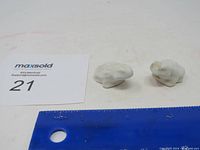 Two small white ceramic frog figurines placed next to a ruler showing their small size, also showing minor dirt marks on one figurine.