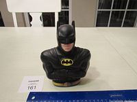 Photo of Batman coin bank bust front view with ruler for size reference showing crossed arms and bat emblem.