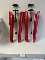 Two red plastic boot trees/shapers with black adjustable handles displayed upright on a white surface against a white background.