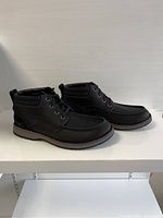 Side angle view of the black lace-up men's ankle boots showing moc toe stitching, padded ankle collar, pull tab at heel, and sole detail with layered colors.