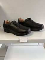 Side view of men's black leather comfort shoes size 43XW on white shelf with lace-up front and cushioned collar.