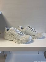 Side profile of men's white FILA sneakers on a neutral background, showing design details including upper, laces and sole pattern.