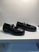 Side angled view showing profile of both black Orthofeet Mary Jane shoes with strap, padded collar, and low heel.