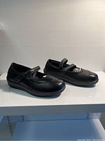 Side angle showing pair of black Mary Jane style shoes with strap and cushioned interior.