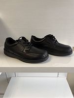 Side angle view of pair of brand new black Orthofeet men's shoes size 11 wide, showing leather upper and laces.