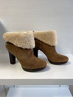 Side view of the brown suede UGG boots with shearling folded cuff and stacked high heel.