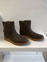Side angled view of both brown UGG ladies boots showing outer side zipper and buckle strap detail.