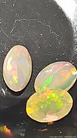 Close-up of three oval Ethiopian opal gemstones displaying rolling flash and play-of-color on black background.