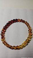 Photo of gradient Baltic amber bracelet on white background showing color transition from dark red amber to yellow amber.