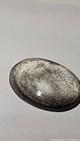 Oval-shaped polished silver sheen obsidian gemstone with notable metallic flash and smooth glossy surface shown from different angles.