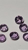 Seven round pink purple amethyst gemstones arranged on white background showing facets and reflective surfaces