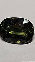 Close-up image of oval cut green sapphire with dark to medium green color tones, showcasing natural inclusions and facets.