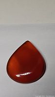 Photo of polished teardrop-shaped carnelian gemstone showing deep red-orange color in ambient light