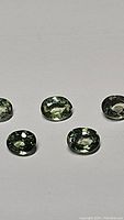 Five oval mint green sapphire gemstones laid out on a white surface showing clarity and color