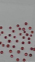Photo showing a spread of small round pink sapphires scattered on a flat surface