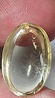 Close-up image of the oval citrine cabochon showing its light yellow color and internal inclusions, natural surface texture, and minor edge wear.