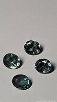 Four oval cut denim blue sapphires laid out on a flat surface, showing facets and color variations.
