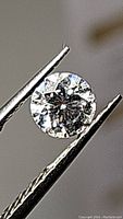 Close-up front view of the round cut 0.50ct Moissanite gemstone held by tweezers showing bright brilliance and facets reflecting light