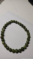 Dark green jade round bead bracelet on white background showing beads uniformly sized and glossy.