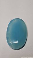 Oval light ice blue chalcedony cabochon gemstone on plain background showing color and shape details.