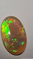 Close-up of the oval 2.58ct Ethiopian opal with bright green, blue, and orange fire colors on polished face visible.