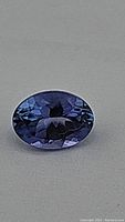 Top-down view of loose oval cut tanzanite on grey background showing table and crown facets and color