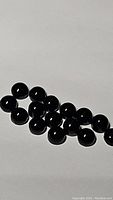 Fifteen round cabochon jet black onyx stones arranged on a plain surface.