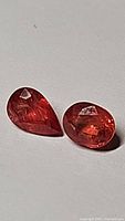Two loose mandarin orange sapphire gemstones, one pear cut and one oval cut, laying flat on a neutral background with visible facets and internal clarity.
