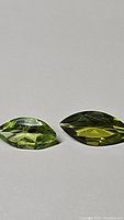Two marquis cut apple green natural peridot gemstones side by side on a plain surface.